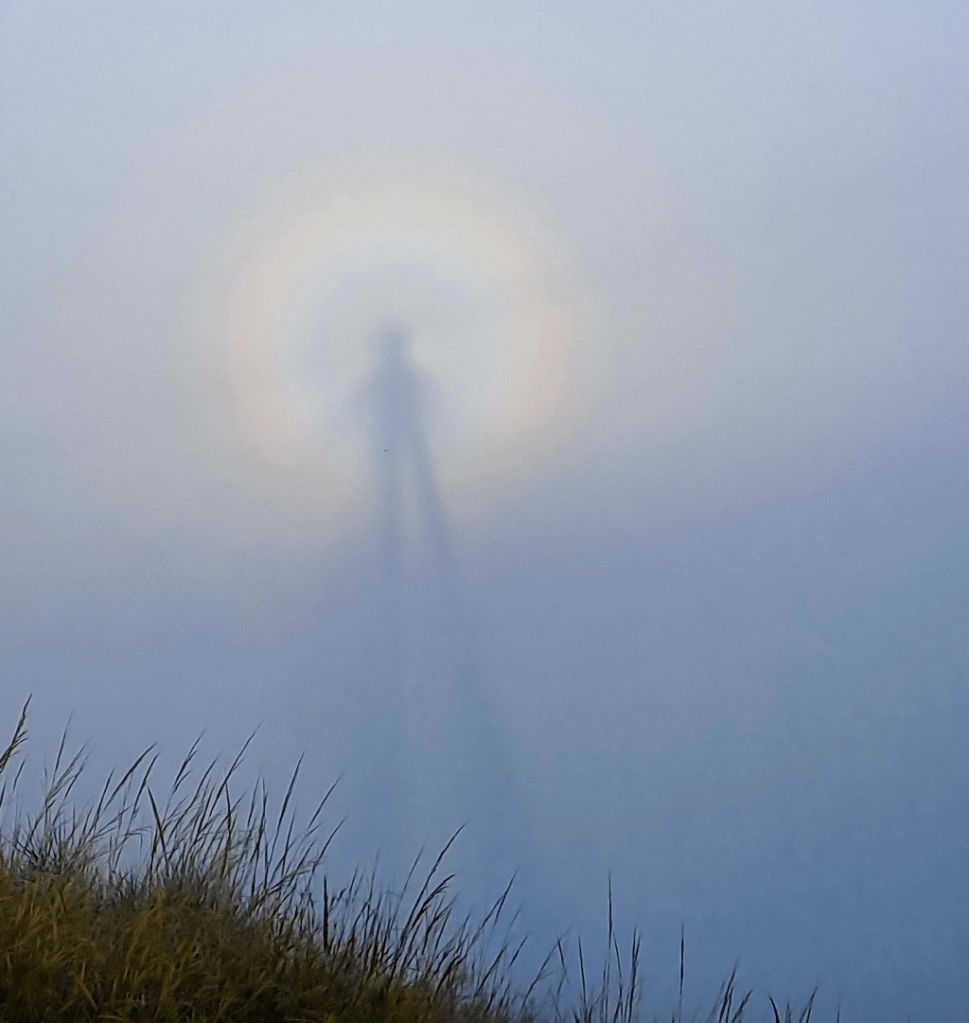 Un'ombra proiettata nella nebbia con un alone di colori luminosi intorno, catturata in un paesaggio montano.